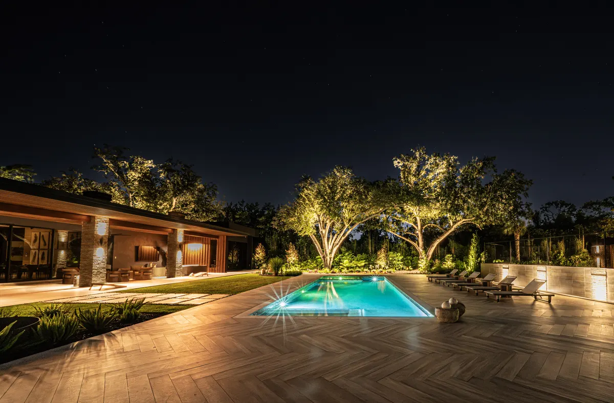 Massive live oak with canopy lighting spreading over a pool and lanai at night