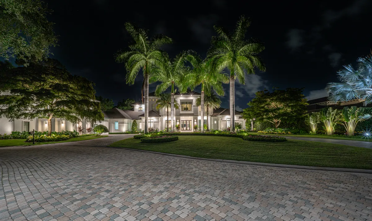 Naples estate at night with towering uplit royal palms flanking a paver drive court