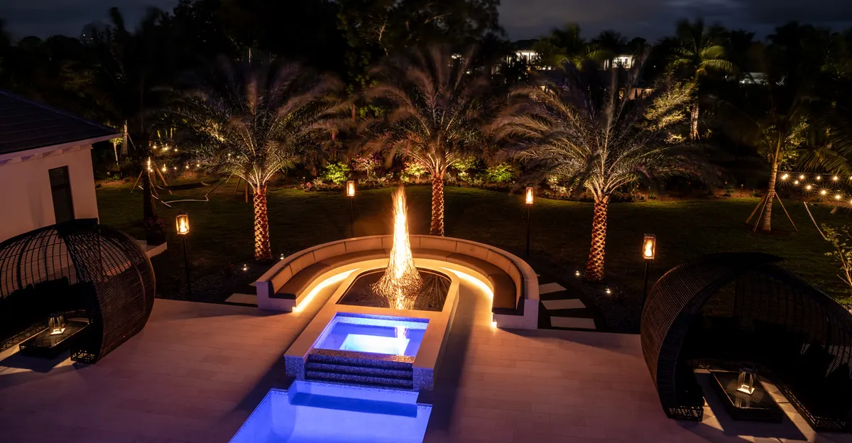 Backyard at night with lit fire feature, glowing spa, and illuminated palm canopies