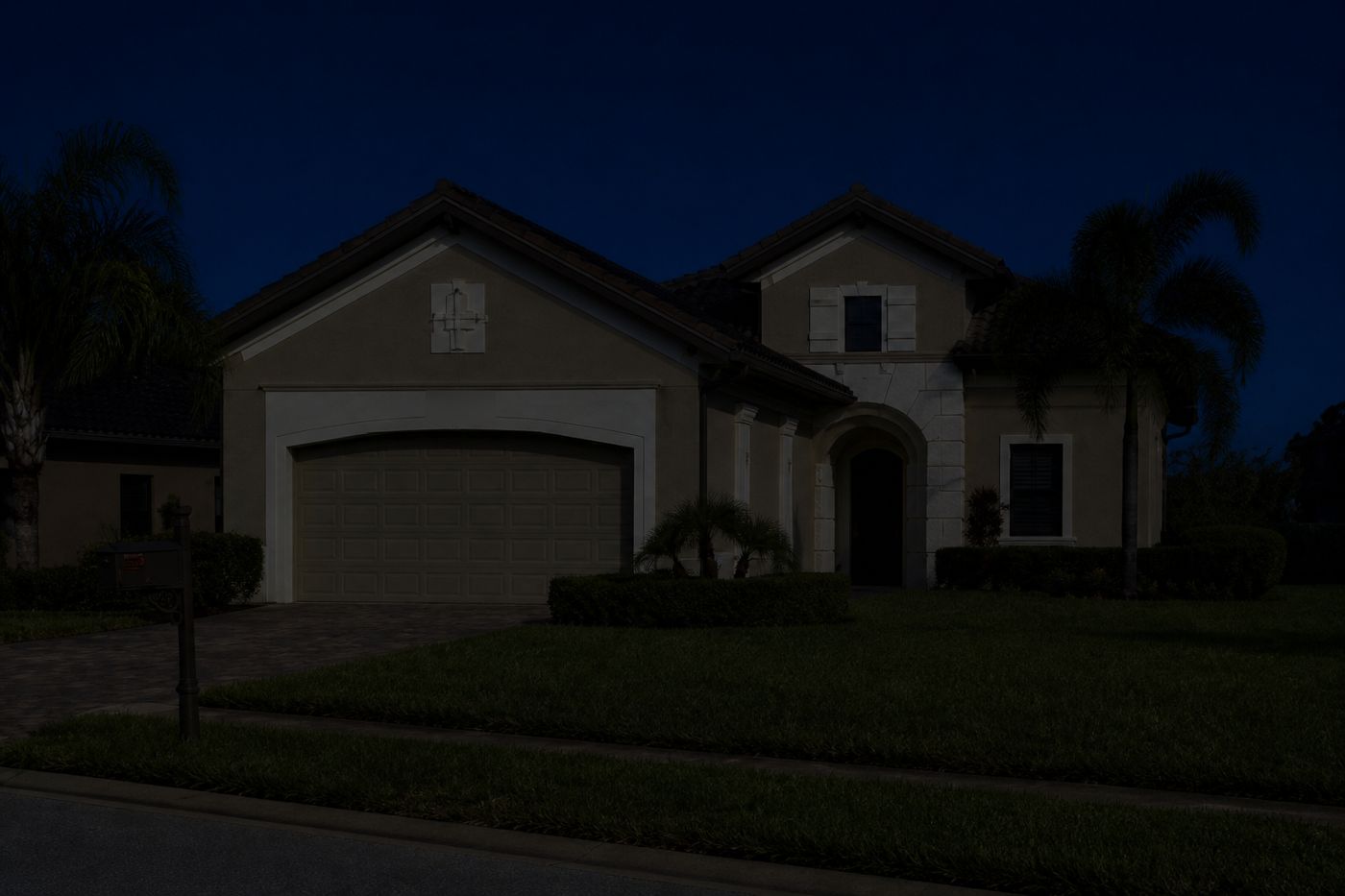 The same home at night with no landscape lighting — the architecture and palms disappear into the dark.