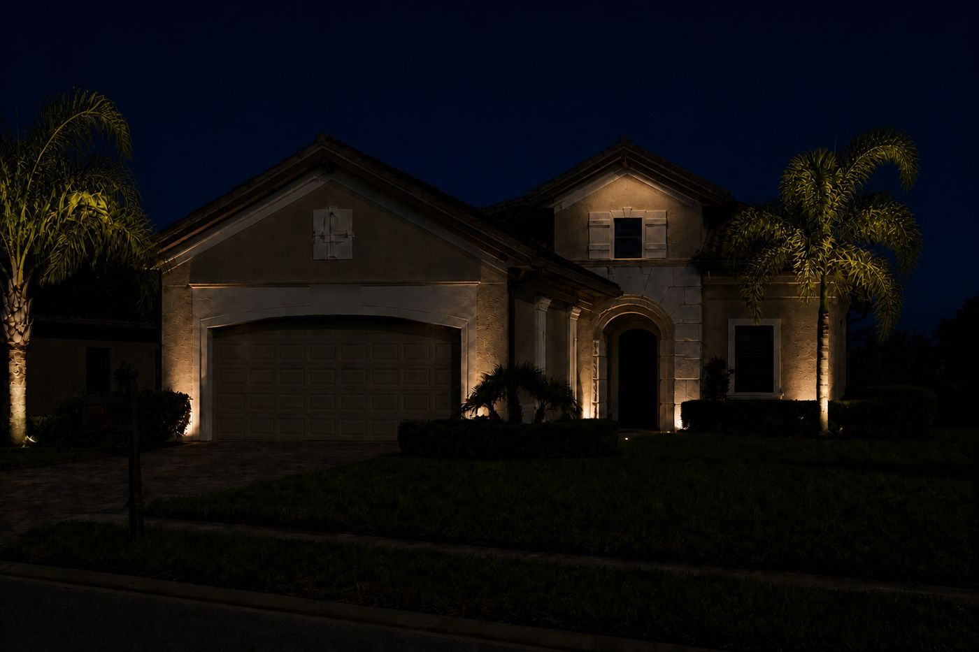 The same home with a Spectrum Nightscapes design: entry and garage flanked symmetrically, palms uplit at trunk and crown, warm 3000K light.